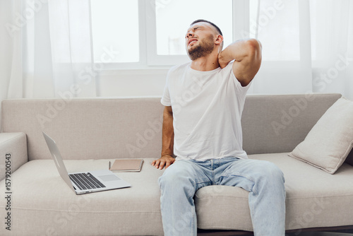 A man experiencing discomfort while working from home, surrounded by technology, highlighting the challenges of work-life blur, mental health, and emotional minimalism.