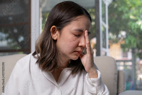 A woman sits on a couch, visibly distressed, with her hand on her forehead, suggesting feelings of stress or anxiety in a calm indoor setting.