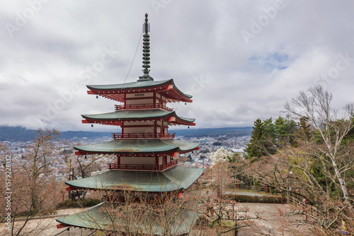 Stunning red pagoda overlooking Hakone, Japan.  Cherry blossoms in the foreground add vibrant color against the cityscape and mountain backdrop. A picturesque spring scene.