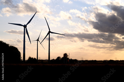 Sunset silhouettes of wind turbines, nature trees and field copy space