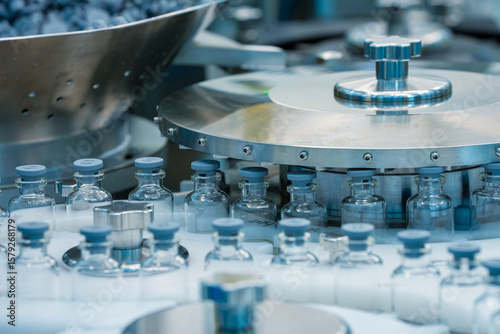 injection vaccine vials in a machine, manufacturing vaccines injections, glass ampoule vial in a healthcare pharmaceutical factory making process blue light with latest hi tech machinery	