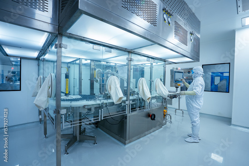 pharmaceutical worker using large machine. person checking operating large machine. medicine making factory. person wearing a ppe kit in a factory. healthcare concept. Pharmaceutical industry. vials