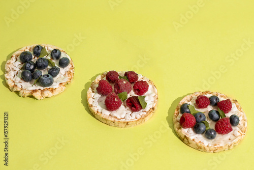 Rice cakes with different types garnish fruits, on green background. Healthy colorful food. Crispy puffed rice cakes with fruit and honey