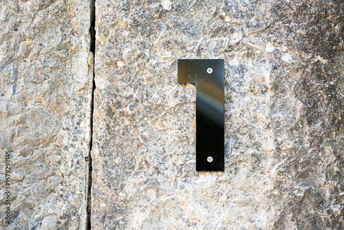 Modern metallic number 1 mounted on a rugged stone wall. The sleek, reflective surface contrasts with the textured background, ideal for architectural or urban design themes photo