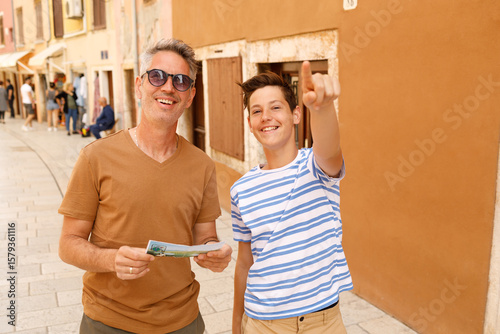 A father and son on a sightseeing trip in Rovinj, Croatia. . They are holding a map. Both appear cheerful and curious, enjoying their time exploring the city together.	
