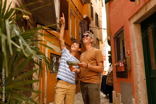 A father and son on a sightseeing trip in Rovinj, Croatia. . They are holding a map. Both appear cheerful and curious, enjoying their time exploring the city together.	
