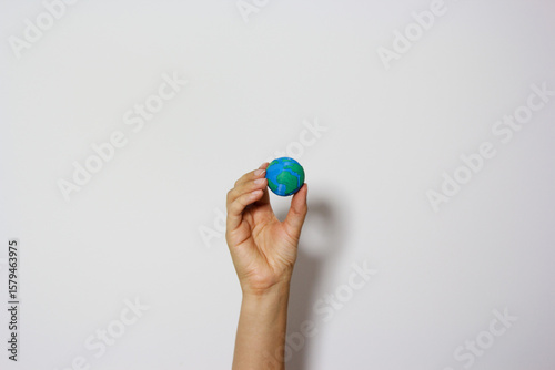 Single hand reaching up holding miniature Earth globe against neutral background, symbolizing environmental aspirations and global responsibility. Planet earth. Earth day concept. Save the planet