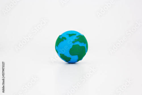Miniature Earth globe model with blue oceans and green continents sitting alone on clean white surface background. Earth day concept. Environmental conservation. Global unity concept. 
