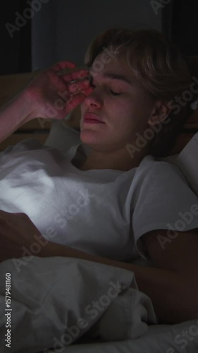 Tired young woman reads news on smartphone lying in bed