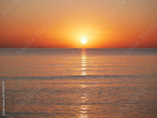 Vivid sunset over the sea with a glowing sun and golden reflection on the calm water. Peaceful and captivating atmosphere. Nature background, relaxation concept, travel theme and inspirational visual