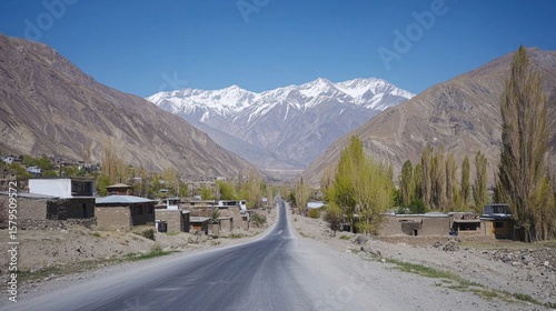 Scenic mountain road through a quiet valley with snow-capped peaks and sparse village houses in autumn