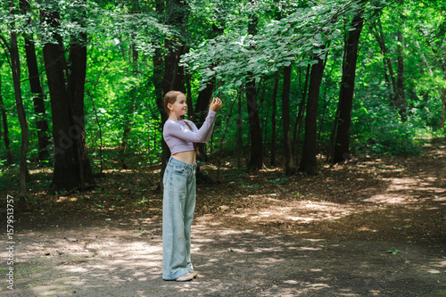 Teenage girl looking at leaves on tree branch in park