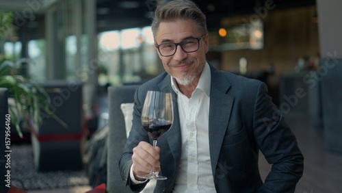 Fotografie Elegant mature businessman smiling and holding glass of red wine, enjoying a moment of relaxation after work