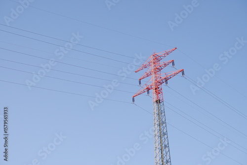 Roter Strommast mit Hochspannungsleitungen vor klarem blauen Himmel