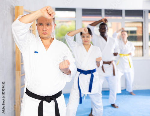 Kata karate teacher conducts classes and performs movements and fighting techniques together with cosmopolite students to prepare them for competitions.
