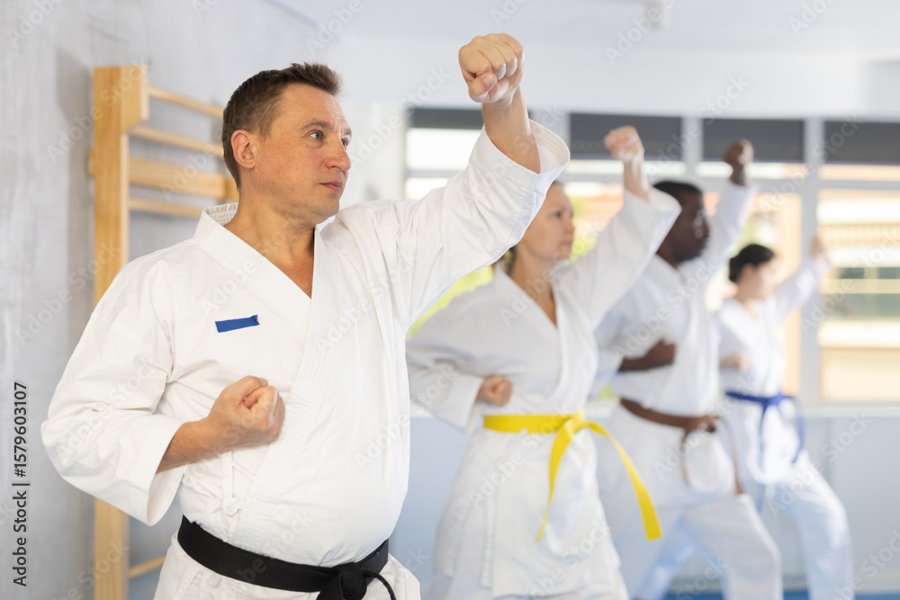 Obraz premium Group of multinational athletic people in kimonos try new fighting techniques at karate lessons