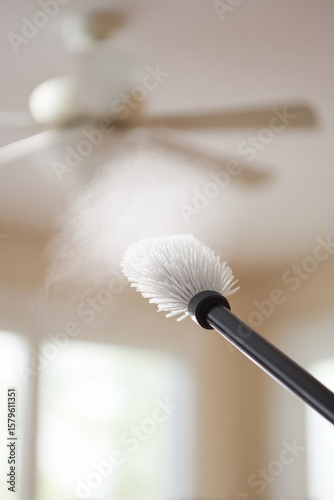 A dusting brush cleans a ceiling fan blade, removing visible dust. Cleaning action, household chore, dust removal