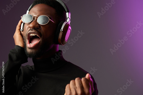 Young Black man singing passionately with headphones, wearing sunglasses and black turtleneck, colorful purple background, capturing the essence of music and emotion