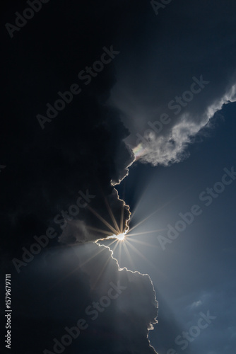 Dramatic sun starburst, breaks through bright, dark, white and blue clouds of thunderstorm   