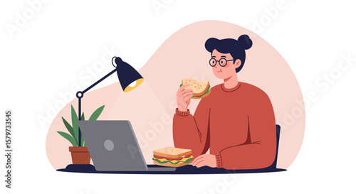 Woman with glasses eating sandwich while working on laptop in cozy home office setup, illuminated by desk lamp