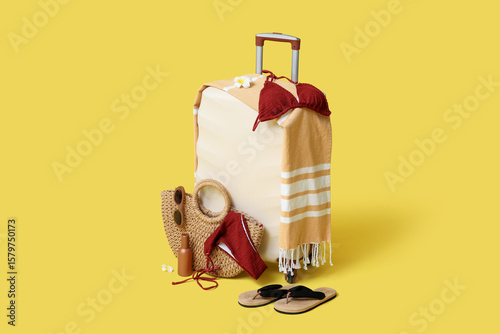 Suitcase, stylish swimsuit and beach accessories on yellow background