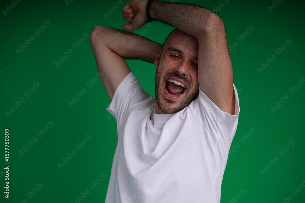 Fototapeta premium Young man with a variety of emotions, wearing a white t-shirt standing against a green background. Studio shot with copy space.