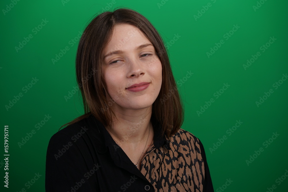 Fototapeta premium A young woman poses in a studio with a green background, showing natural emotions, full of expressions and dynamic movements. Unedited image