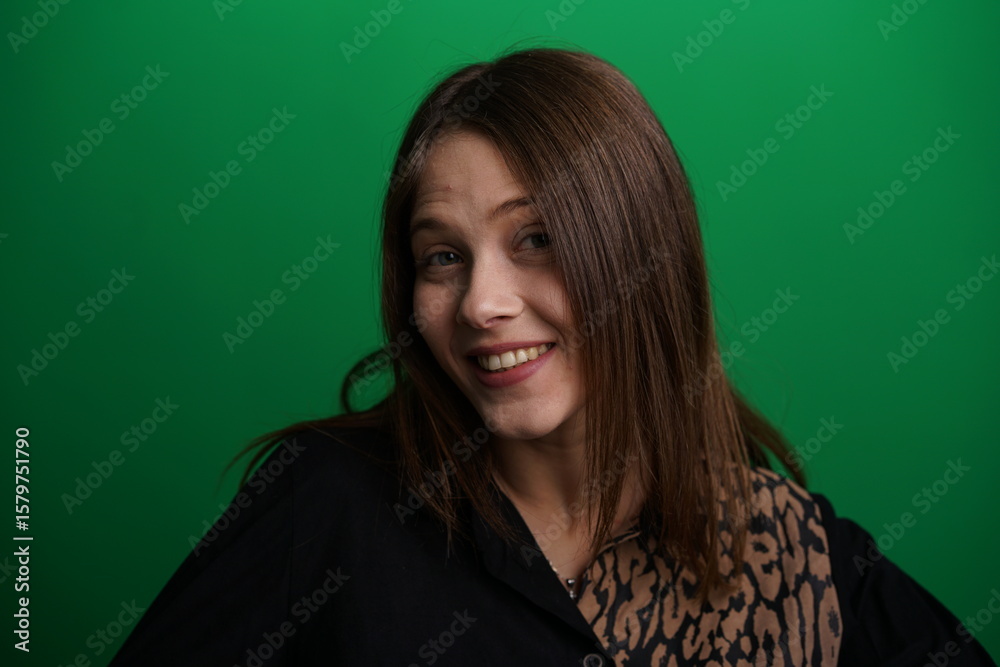 Fototapeta premium A young woman poses in a studio with a green background, showing natural emotions, full of expressions and dynamic movements. Unedited image