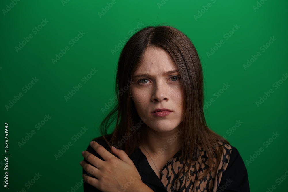 Fototapeta premium A young woman poses in a studio with a green background, showing natural emotions, full of expressions and dynamic movements. Unedited image