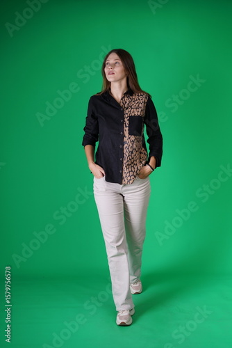 A young woman poses in a studio with a green background, showing natural emotions, full of expressions and dynamic movements. Unedited image