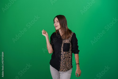 A young woman poses in a studio with a green background, showing natural emotions, full of expressions and dynamic movements. Unedited image