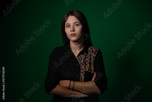A young woman poses in a studio with a green background, showing natural emotions, full of expressions and dynamic movements. Unedited image