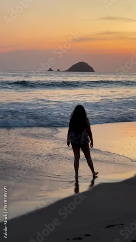 Mexican woman walks in the beach, stops and gazes at the sunset