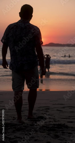 Man's sihouete walks in the beach to the sunset, stops and go away