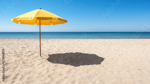 Vibrant yellow beach umbrella stands alone serene sandy beach, casting soft shadow warm sand