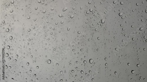 A macro capture of wet blue raindrops on a transparent glass window surface creates an abstract liquid texture