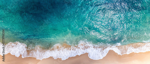 A vibrant turquoise wave curls and crashes towards the shore under a clear blue sky. The energy of the ocean is captured in motion, showcasing the raw beauty and power of nature. Perfect for themes of
