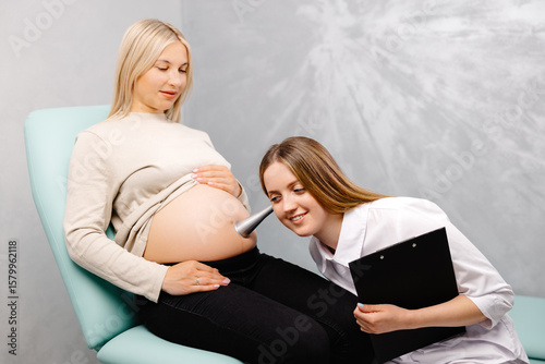 A gynecologist leans a stethoscope to a pregnant woman's belly and listens to the baby's heartbeat photo