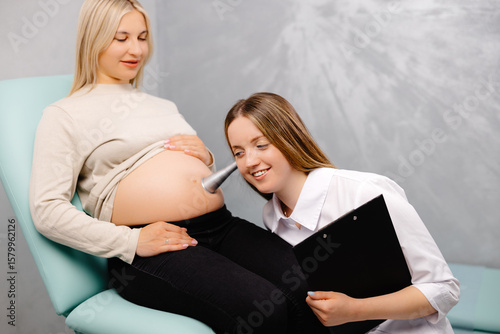 A gynecologist leans a stethoscope to a pregnant woman's belly and listens to the baby's heartbeat photo
