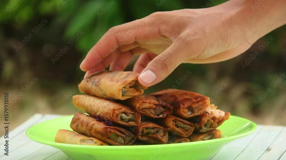A man peeling food made from purple sweet potato covered with spring roll skin, home-made food made from purple sweet potato arranged on the table