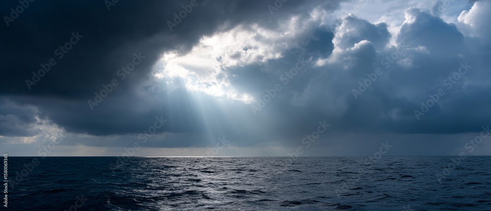 Fototapeta premium Sunlight streaming through dramatic storm clouds over calm ocean water, creating peaceful and moody atmosphere