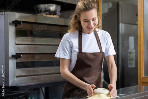 A young woman in a brown apron is preparing dough on a work surface