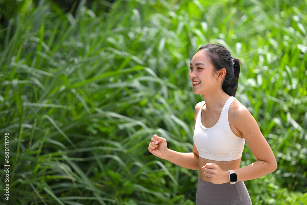 Fototapeta premium Fit Asian woman jogging among lush greenery under bright natural light