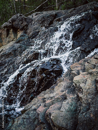 A waterfall is flowing down a rocky cliff. The water is clear and the rocks are grey. The scene is peaceful and serene
