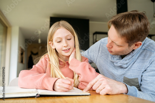 Father assisting daughter in doing homework at table