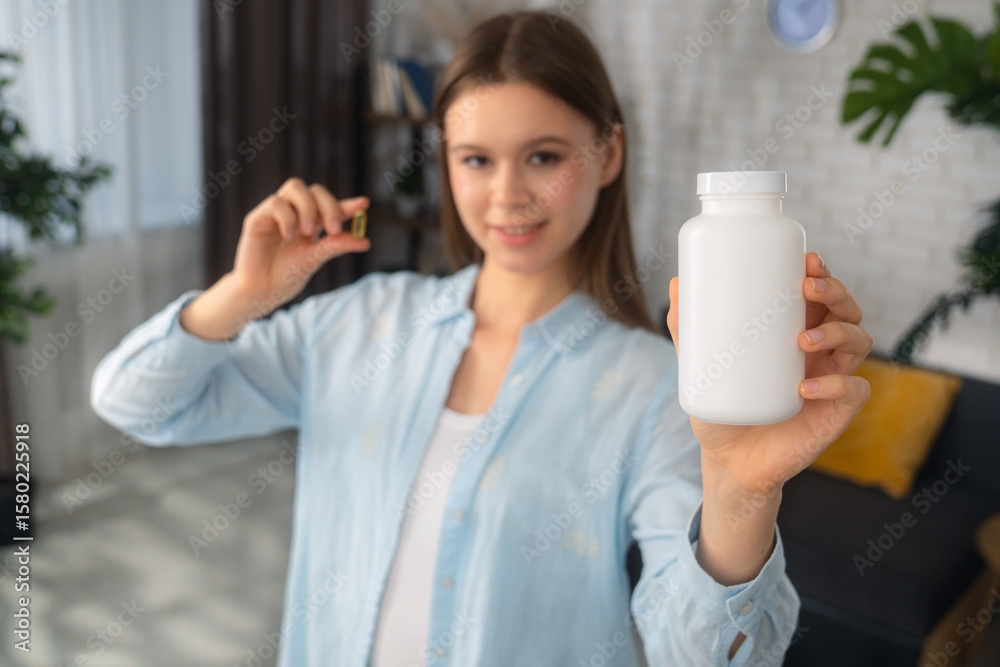 Young Woman Holding Bottle and Capsule in Bright Home Setting Young Woman Holding Bottle and Capsule in Bright Home Setting