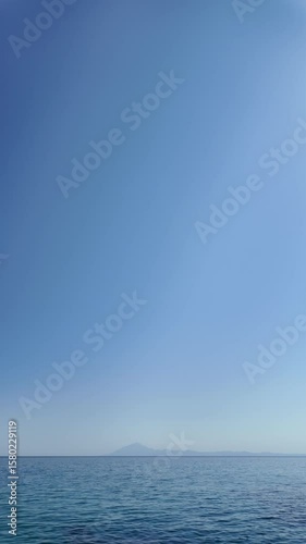 Aerial view of sea waves, sky, mountains, and sand.