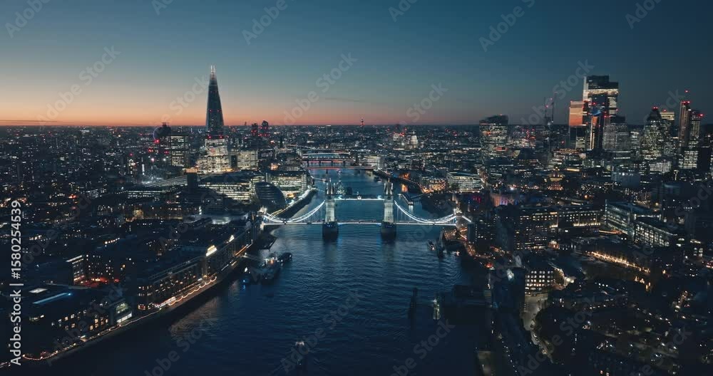 London: Aerial view of city illuminated skyline at sunset, iconic Tower Bridge, The Shard, and night cityscape stretching along the River Thames. Drone flight footage zoom out panorama. Blue toning
