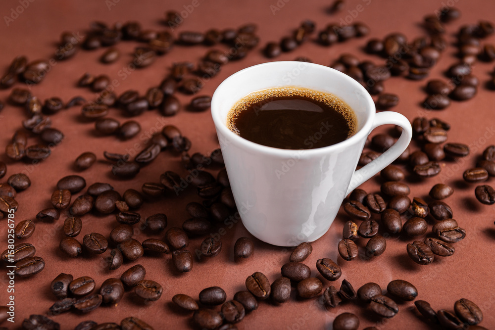 Fototapeta premium A espresso cup filled with dark coffee surrounded by roasted beans on reflective surface.