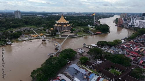 Aerial view of the sarawak state legislative assembly building with golden dome roof and modern pedestrian darul hana bridge crossing the sarawak river